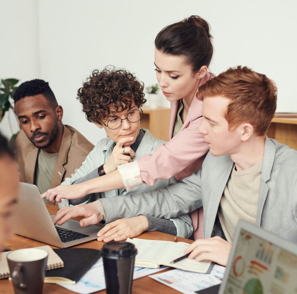 A group of professionals engaged in a collaborative office meeting, discussing ideas with laptops.